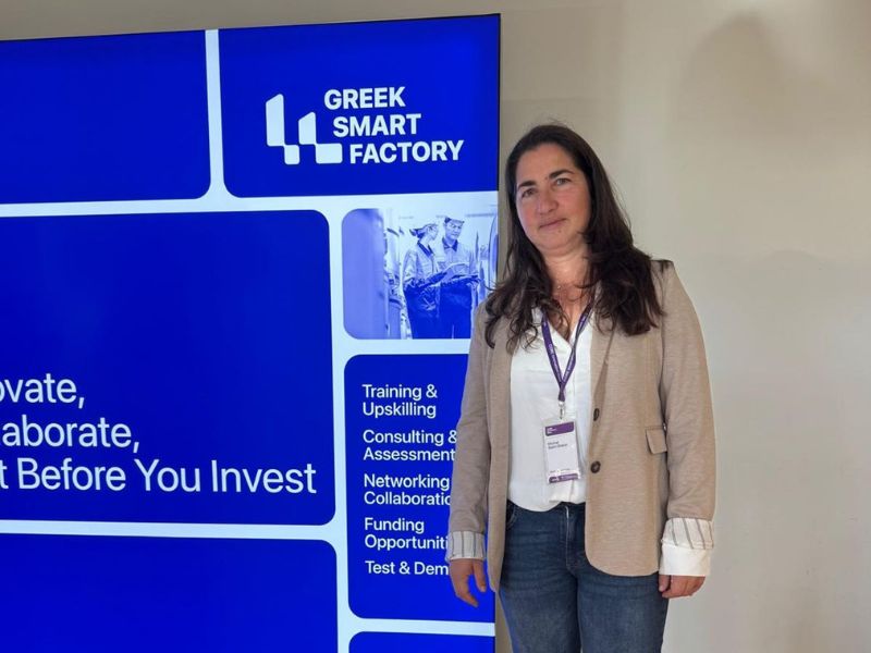 מיכל שטל בעל החברה, עומדת לייד שלט הכנס, בכנס Industry 4.0 באתונה.